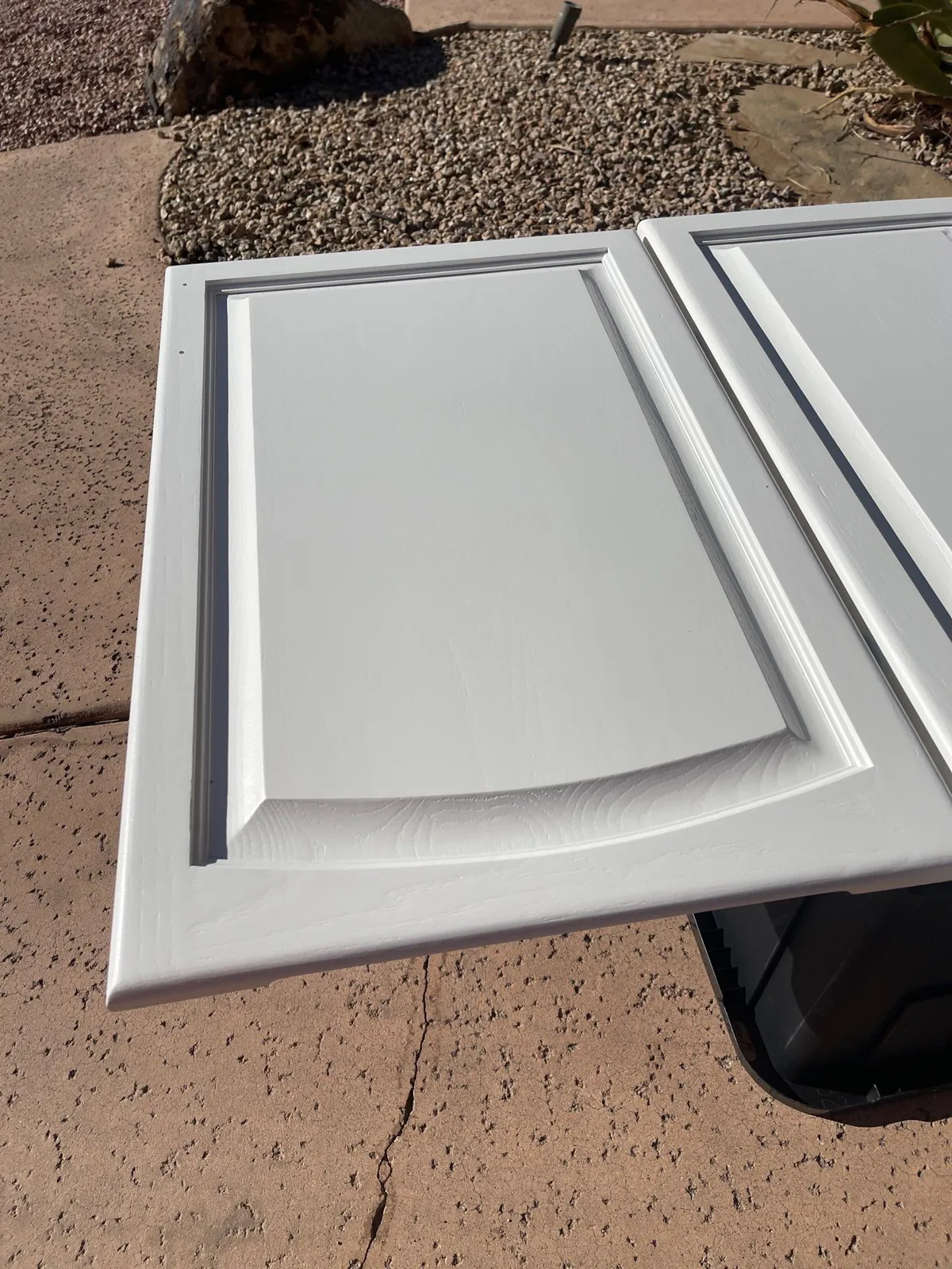 Close-up of a raised-panel cabinet door freshly coated white, resting outdoors