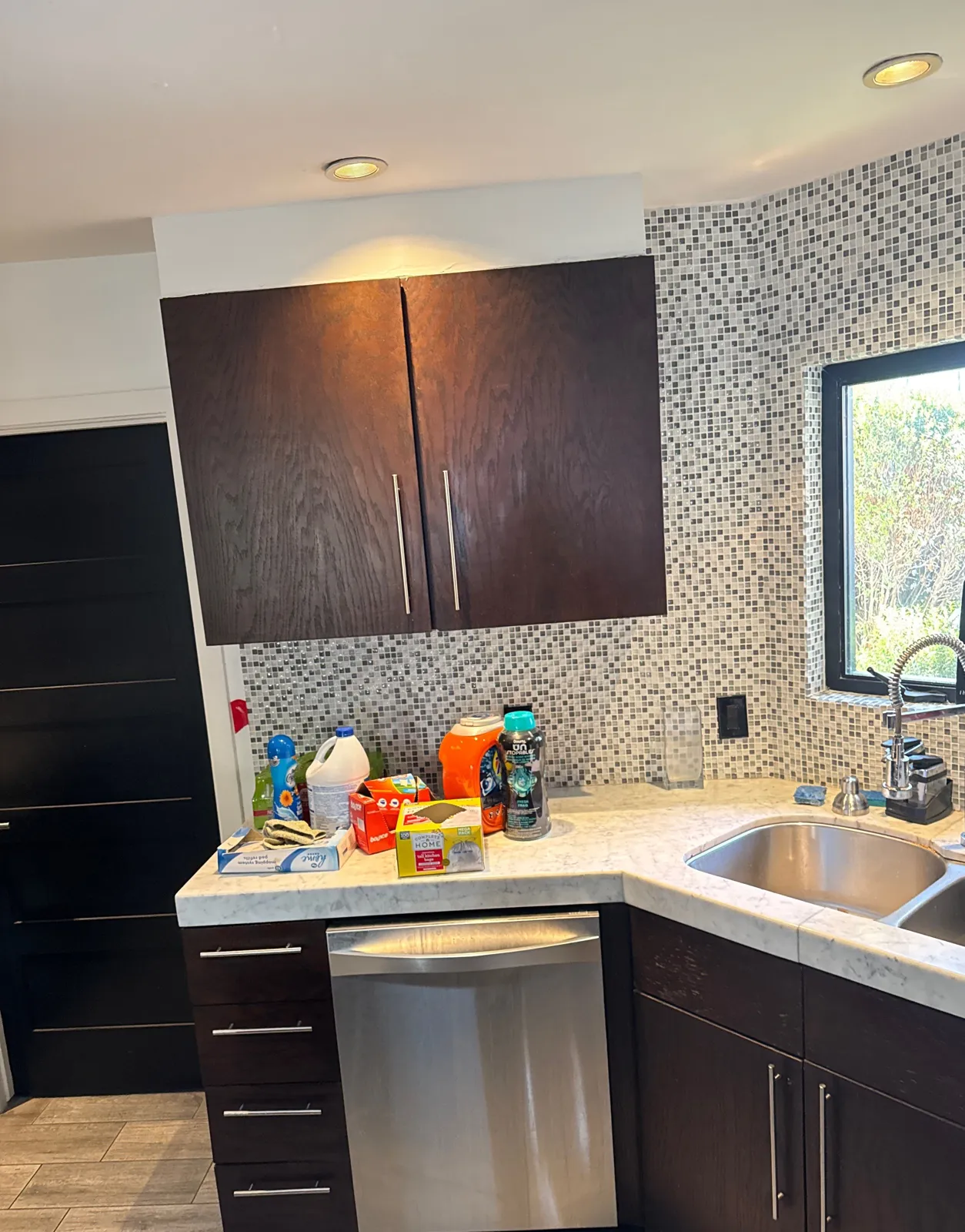 Dark espresso slab cabinets around a dishwasher and corner sink with a mosaic tile backsplash