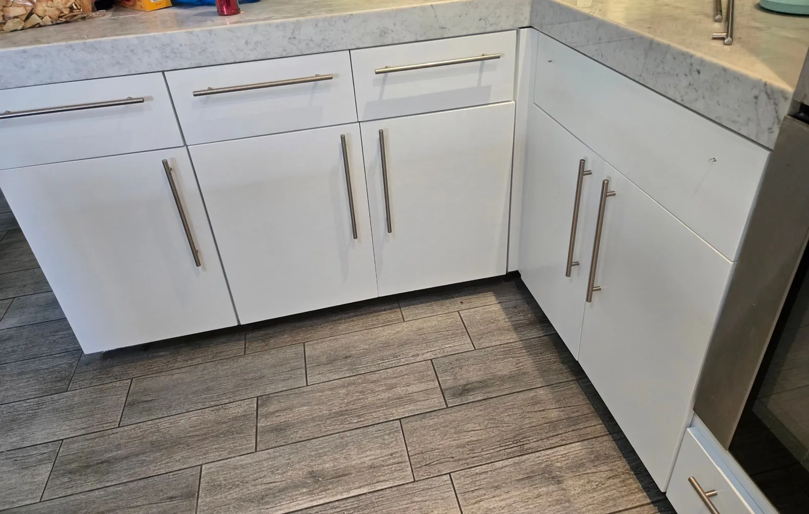 White slab lower cabinets and drawers with stainless bar pulls under a marble-look countertop