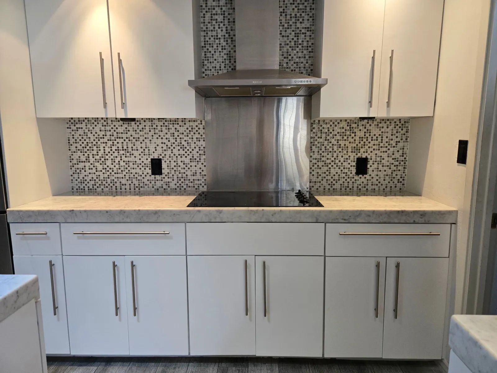 White flat-slab cabinets with long stainless bar pulls around a stainless hood and mosaic backsplash