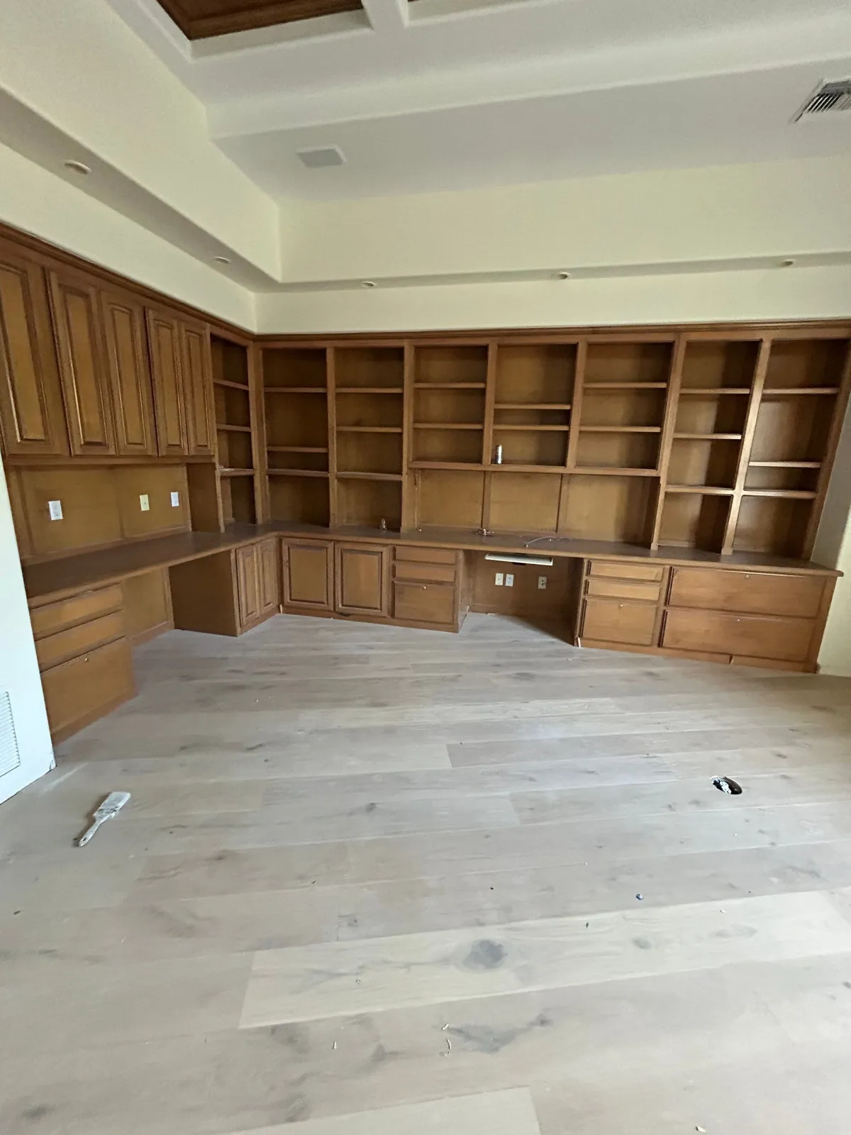 Large L-shaped home office of stained-wood built-in bookcases and desk cabinetry under a coffered ceiling