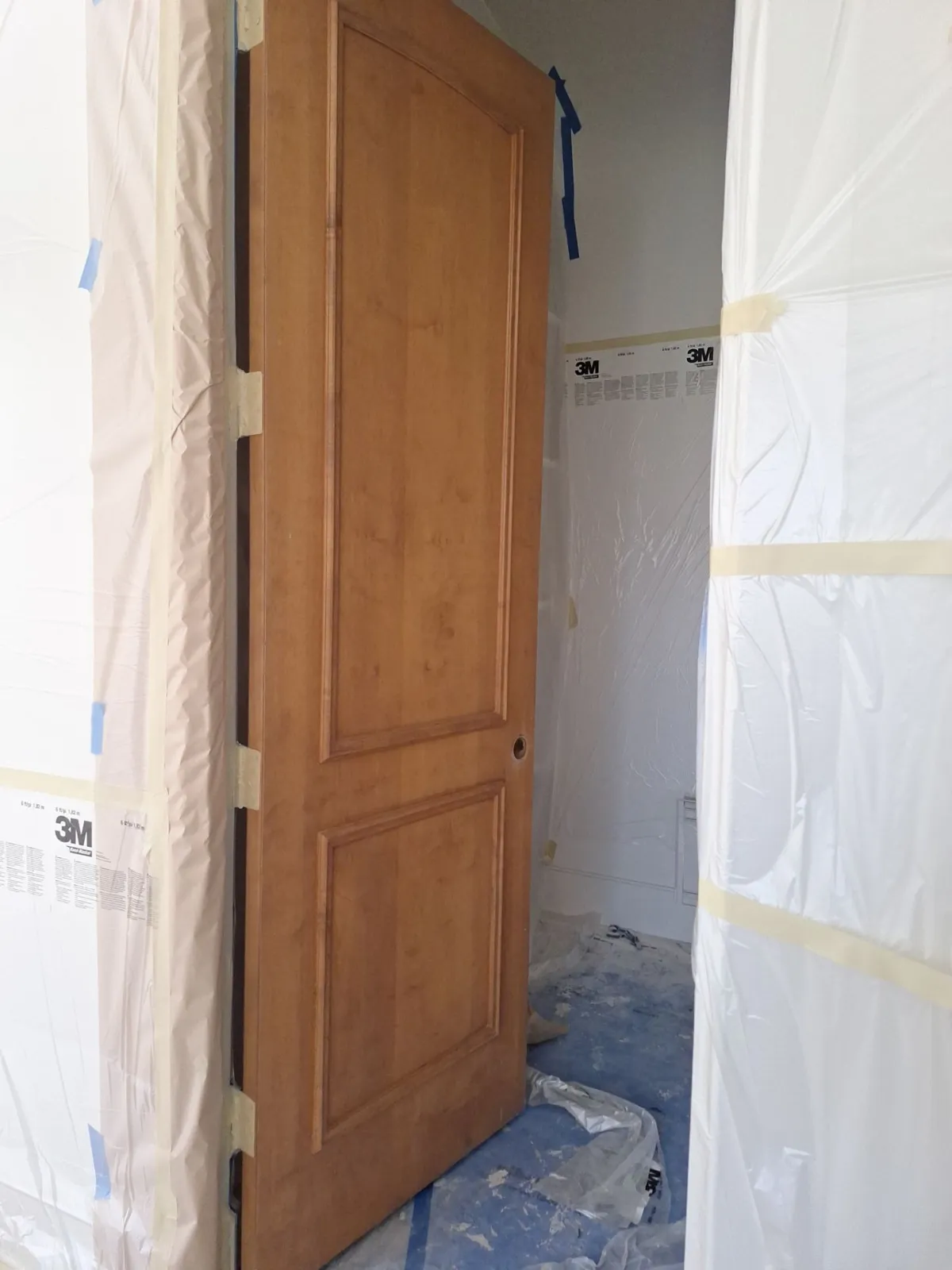 Stained-wood two-panel interior door with surrounding walls masked in plastic for painting