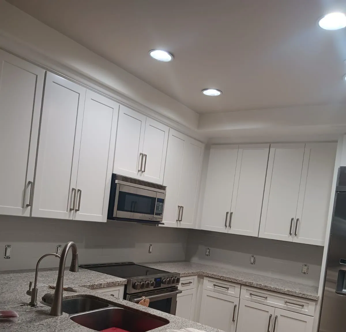 White shaker upper and lower cabinets wrapping a kitchen with a granite island and undermount sink